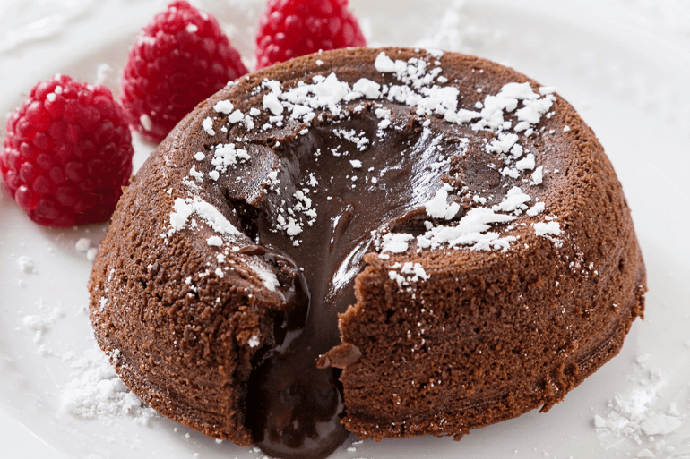 Chocolate oozing out from lava cake and served with 3 raspberries