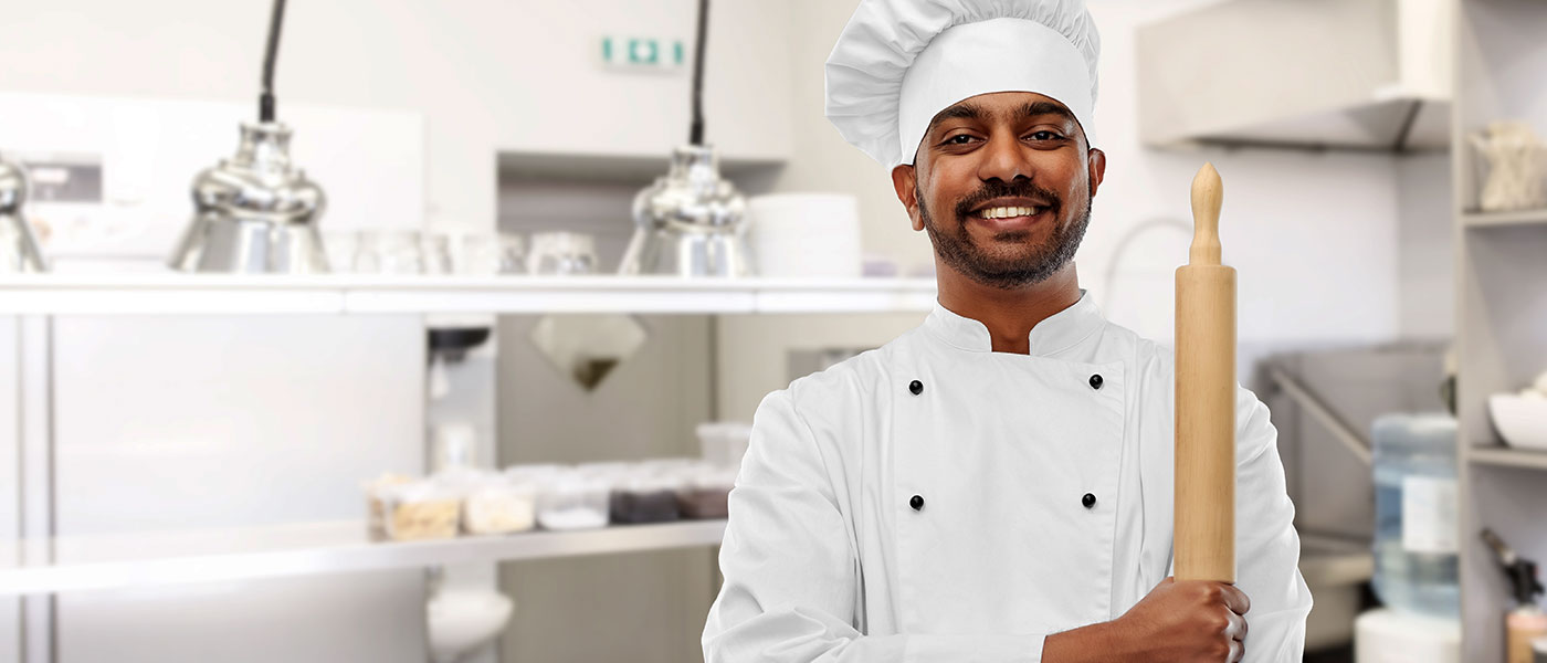 Smiling chef standing in kitchen while holding rolling pin
