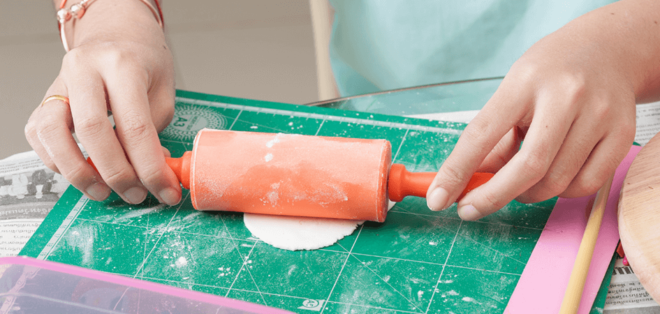 A person using a small rolling pin to flatten out fondant